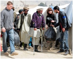 NTM-A/CSTC-A personnel help two afghan amputees with their bags of donated goods. Over 400 bags, which contained clothes, toiletry items, toys, candy, and school supplies, were distributed to several hundred Afghans who live at Qaragha refugee camp.